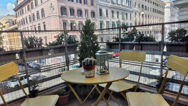 A balcony with a round table and four chairs, overlooking a street with buildings and parked cars. - Hotel Principe Eugenio (Rome)