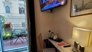 A hotel room with a television mounted on the wall, a desk with a lamp, a chair, and a small table with a remote control and a cup. - Hotel Principe Eugenio (Rome)