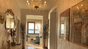 A hallway with a chandelier, a mirror, a vase with dried flowers, a framed picture, and a view of the sea through a window. - Oasis Lagoon Estate (Venice)