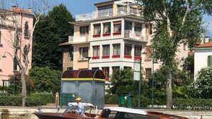 A wooden boat with a man steering, moving through a canal with buildings and trees in the background. - Oasis Lagoon Estate (Venice)