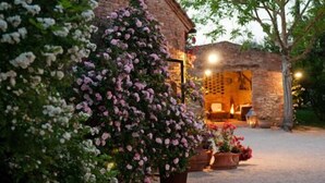Un edificio rustico in pietra con un interno accogliente, circondato da vegetazione rigogliosa e piante fiorite.