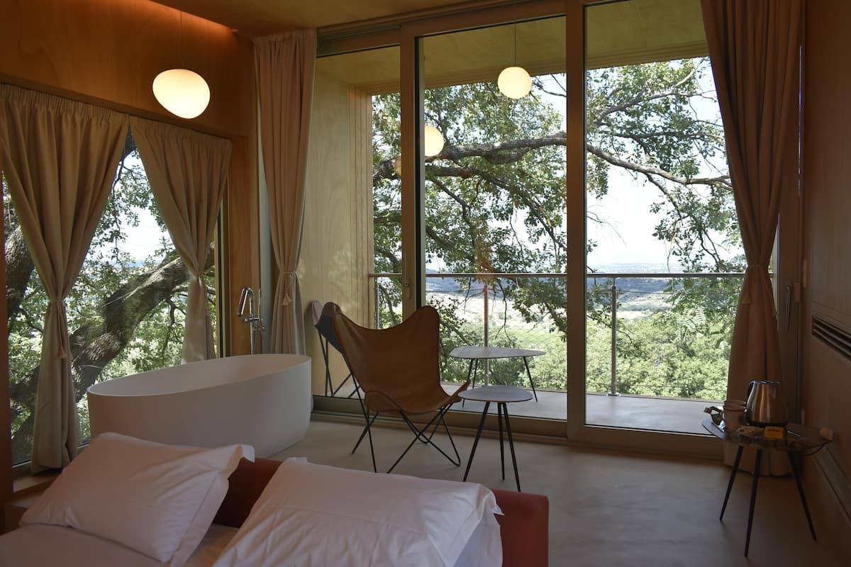 A bedroom with a large window, a bathtub, a chair, and a small table.