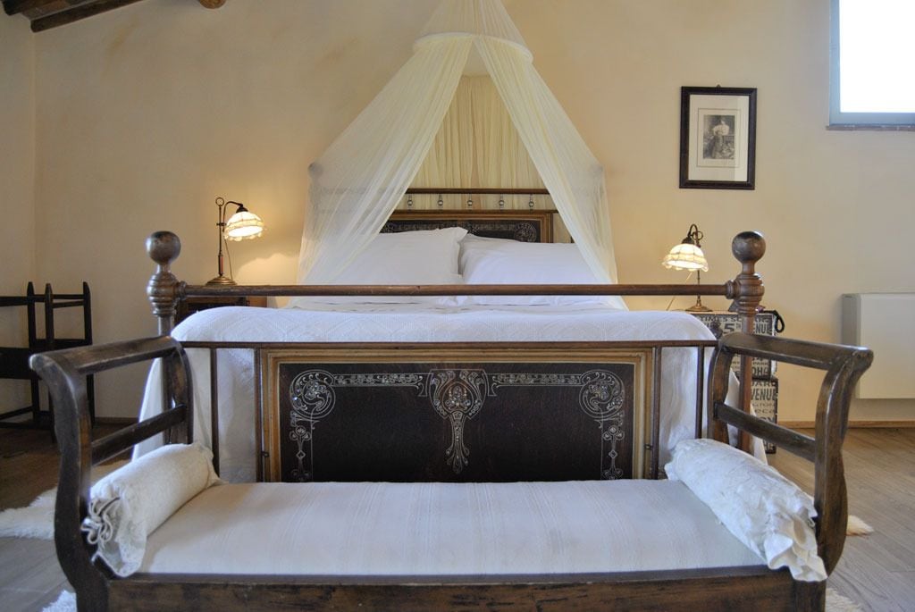 A bed with a canopy, two bedside lamps, a framed picture on the wall, and a rustic wooden headboard.