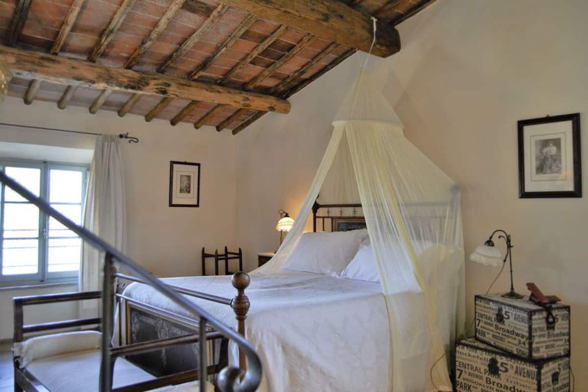 A bedroom with a wooden bed frame, a canopy bed, a staircase, and a nightstand with a lamp.
