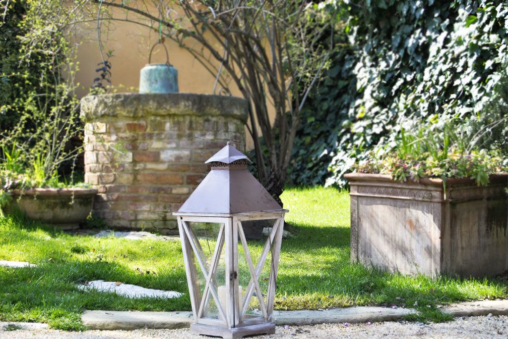 A lantern in a garden with a stone wall and greenery in the background.