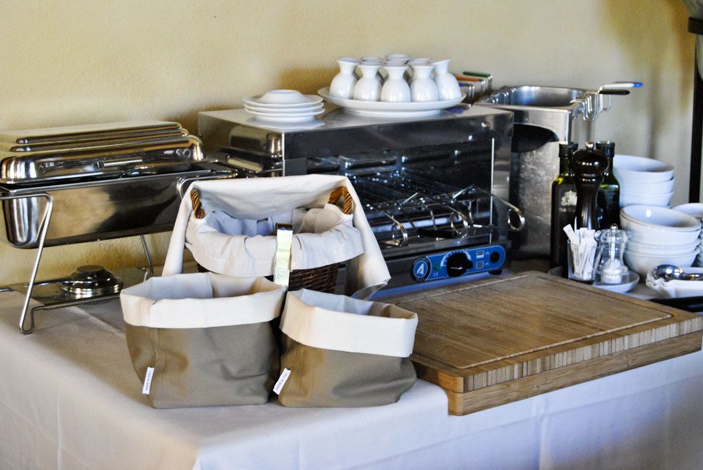 Uma cozinha com fogão, panelas e diversos utensílios. Há também algumas sacolas e uma bandeja sobre a mesa.