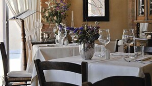 Zona pranzo con tavoli apparecchiati per un pasto, con tovaglie bianche, bicchieri trasparenti e centrotavola floreali.