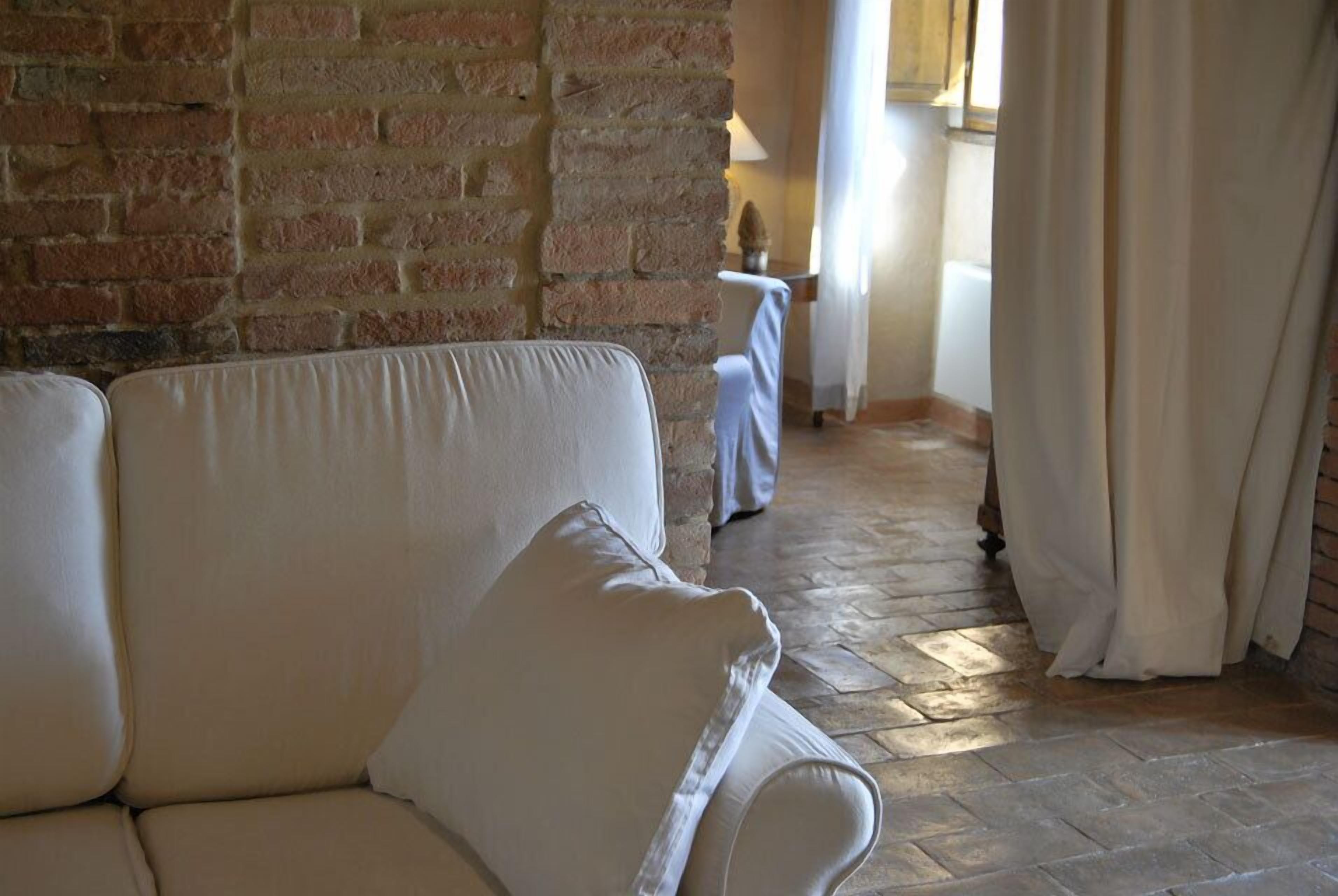 Una habitación con un sofá blanco, una pared de ladrillo y una ventana con cortinas.