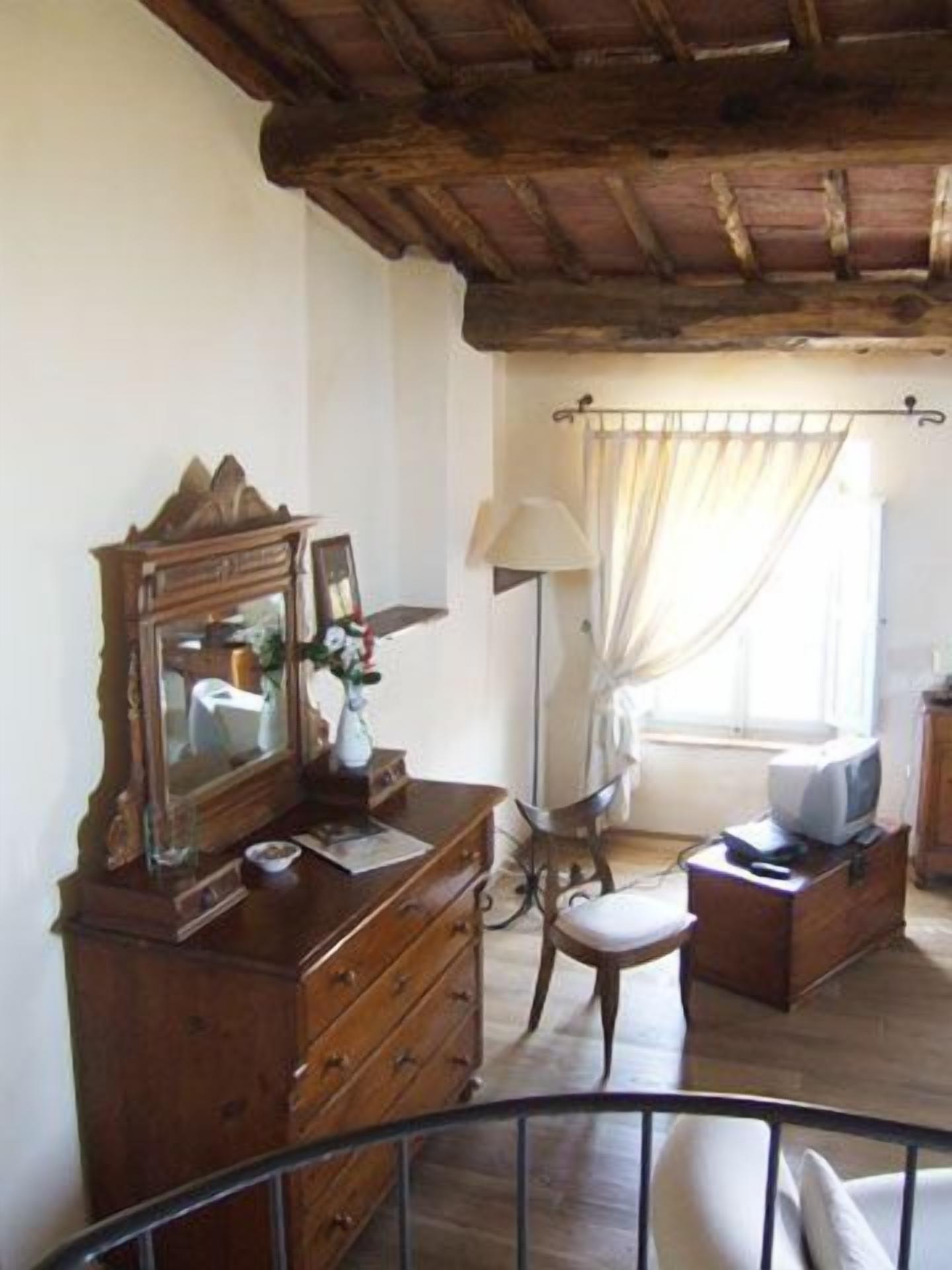 A room with a wooden dresser, a mirror, a television on a wooden cabinet, a chair, and a window with curtains.