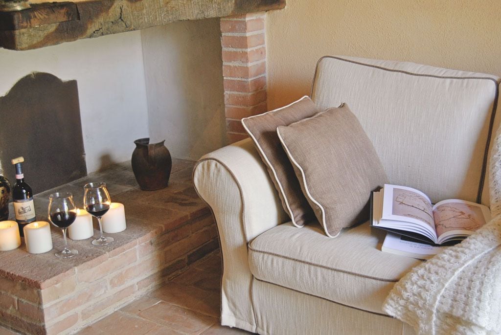 Una habitación acogedora con una zona de estar con cojines, una chimenea, velas y un libro.