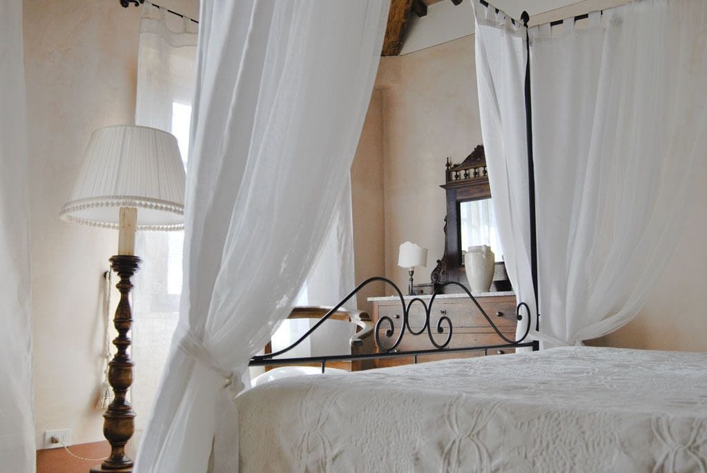 A bedroom with a four-poster bed, a bedside lamp, and a dresser with a mirror.