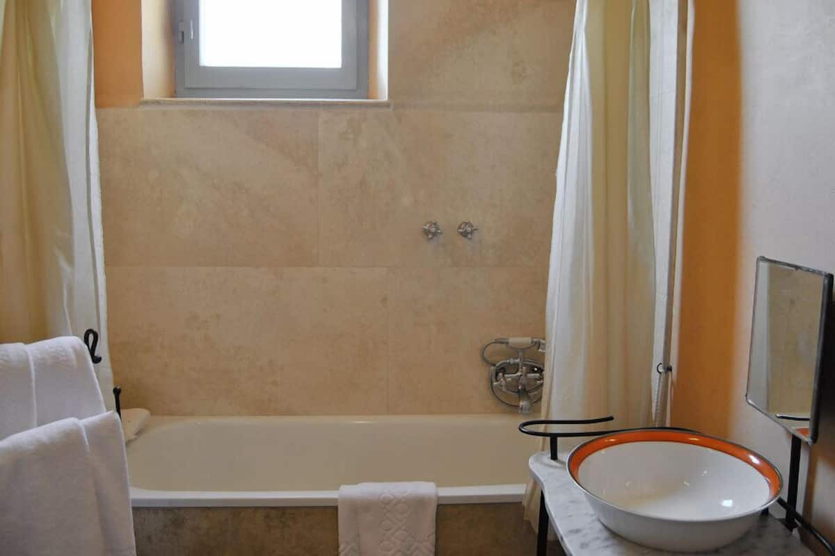 A bathroom with a bathtub, a sink with a bowl, and a window above the tub.