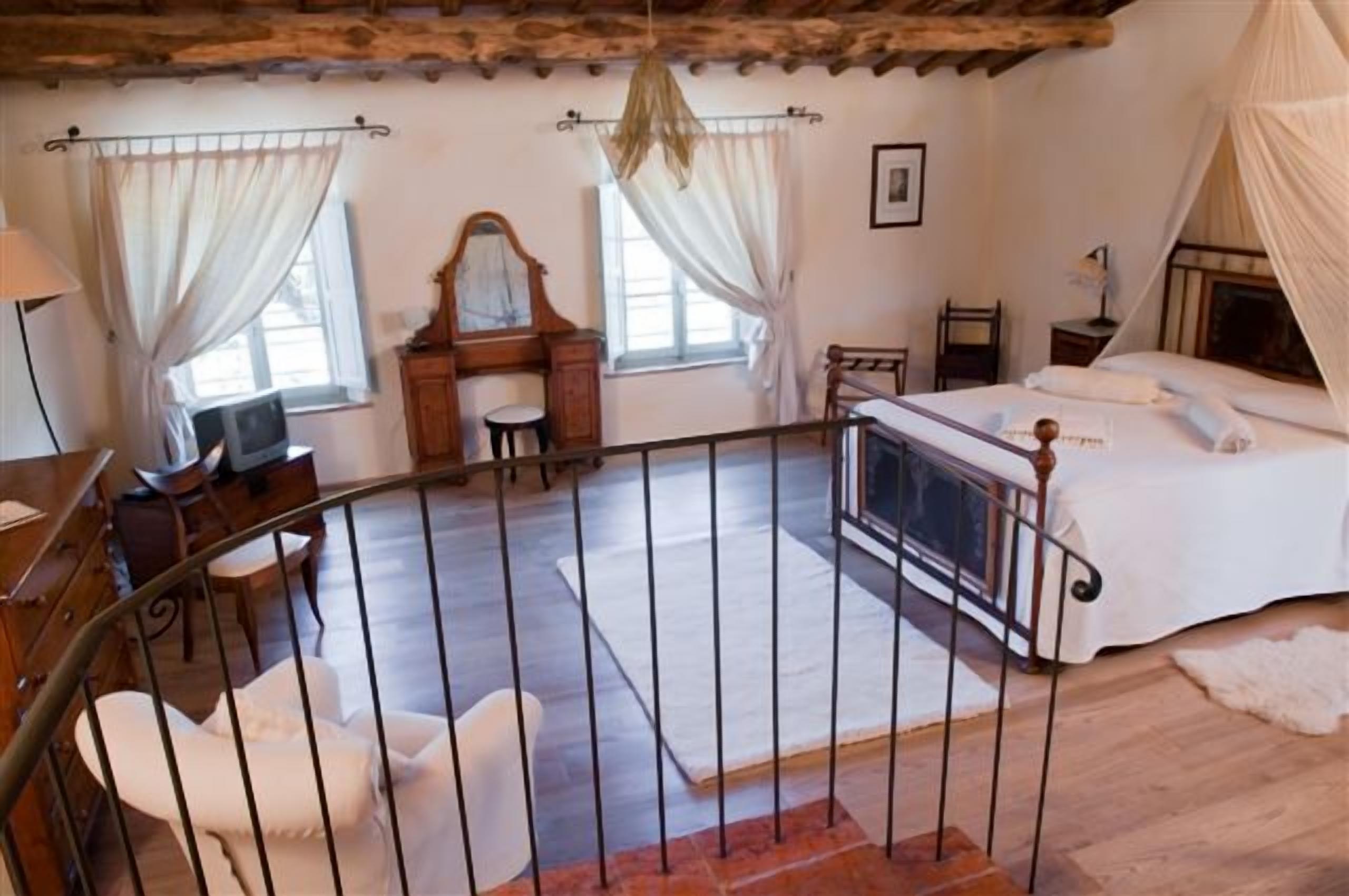 Un dormitorio con cama, escritorio, silla, ventana y barandilla de balcón.