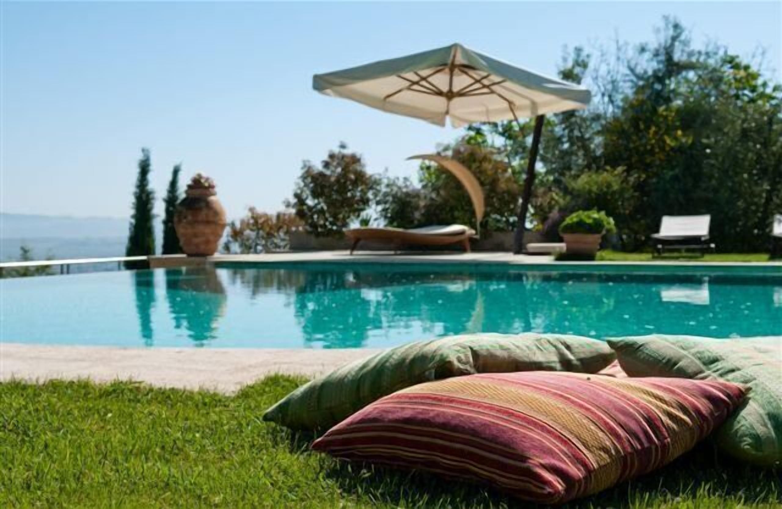 Zona de piscina con una silla de descanso, sombrilla y almohadones decorativos.