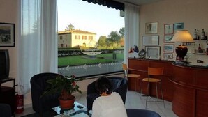 A room with a large window, a desk, a chair, a potted plant, and a lamp.