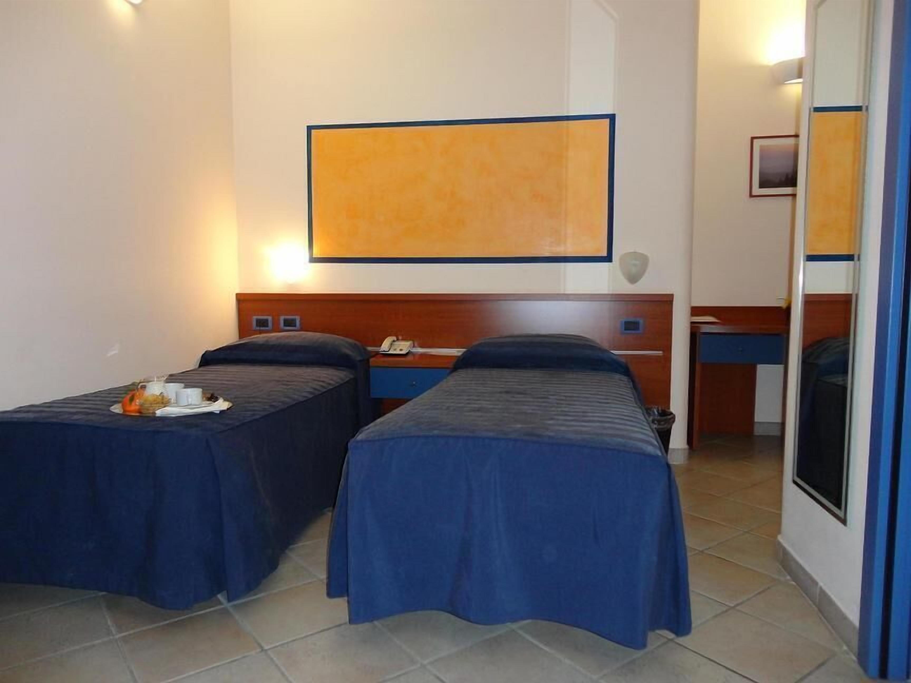 A hotel room with two single beds, a wooden headboard, a small desk, and a large painting on the wall.