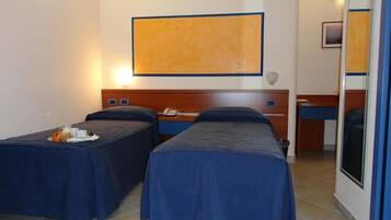 A hotel room with two single beds, a wooden headboard, a small desk, and a large painting on the wall.