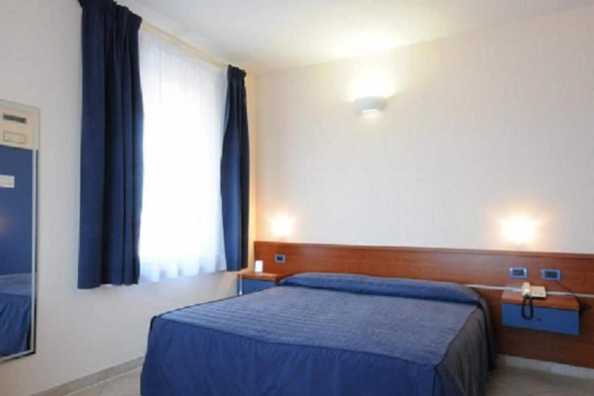 A hotel room with a bed, a nightstand, a telephone, and a window with curtains.