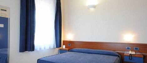 A hotel room with a bed, a nightstand, a telephone, and a window with curtains.