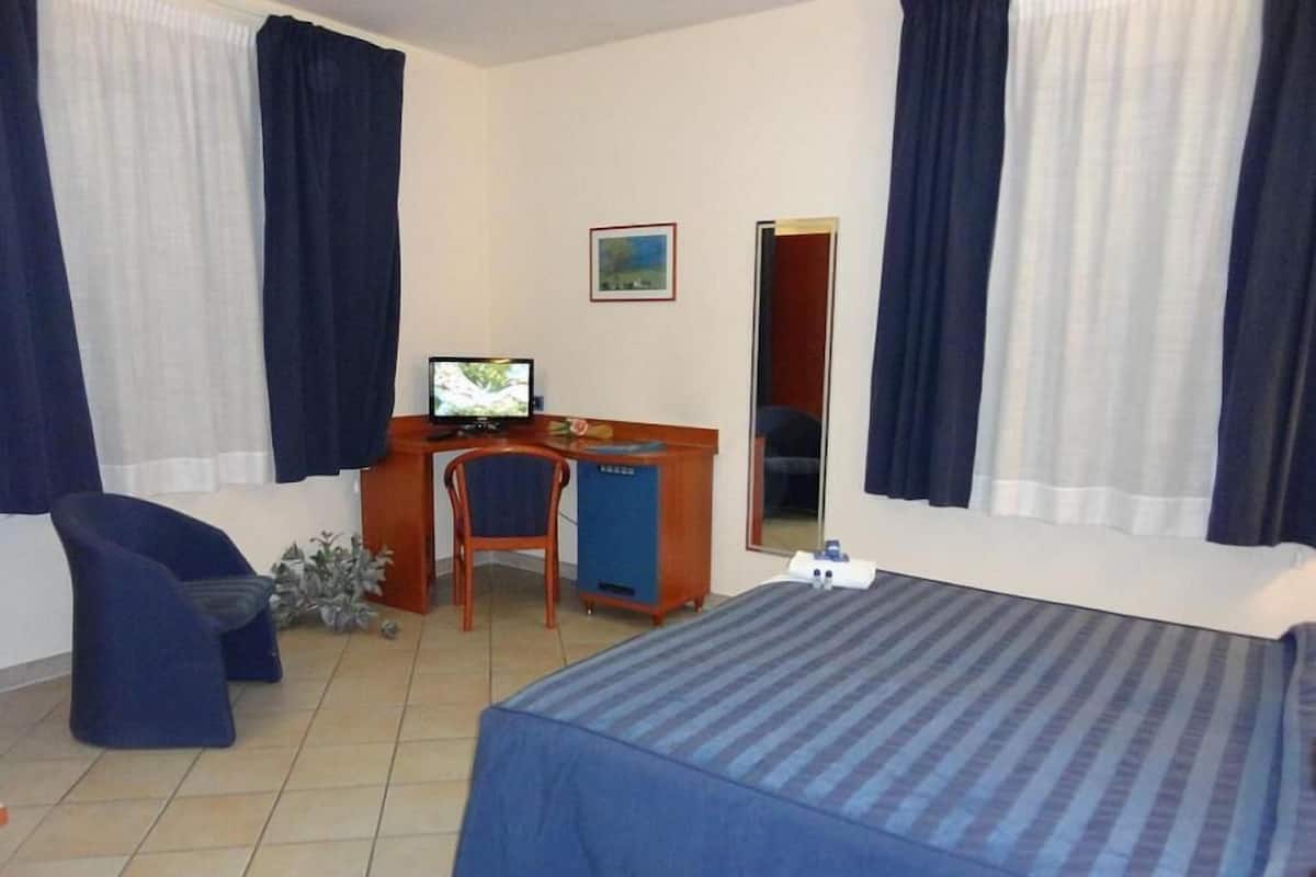 A hotel room with a bed, a desk, a chair, a television, and a window with curtains.