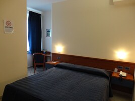 Una habitación de hotel con cama, escritorio, silla y mesita de noche con teléfono.
