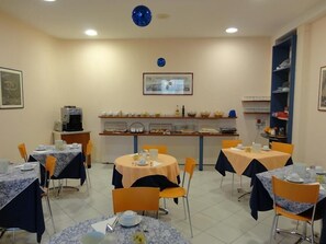 Un comedor con mesas redondas cubiertas con manteles, sillas y una mesa de buffet con alimentos.