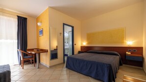 A hotel room with a bed, a desk, a chair, a small table, and a large painting on the wall.