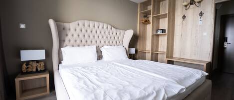 Una cama bien tendida en una habitación de hotel, con cabecera de madera, una mesita de noche con lámpara y un armario con espejo.
