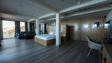 A modern hotel room with a large bed, a desk, a chair, and a wardrobe.