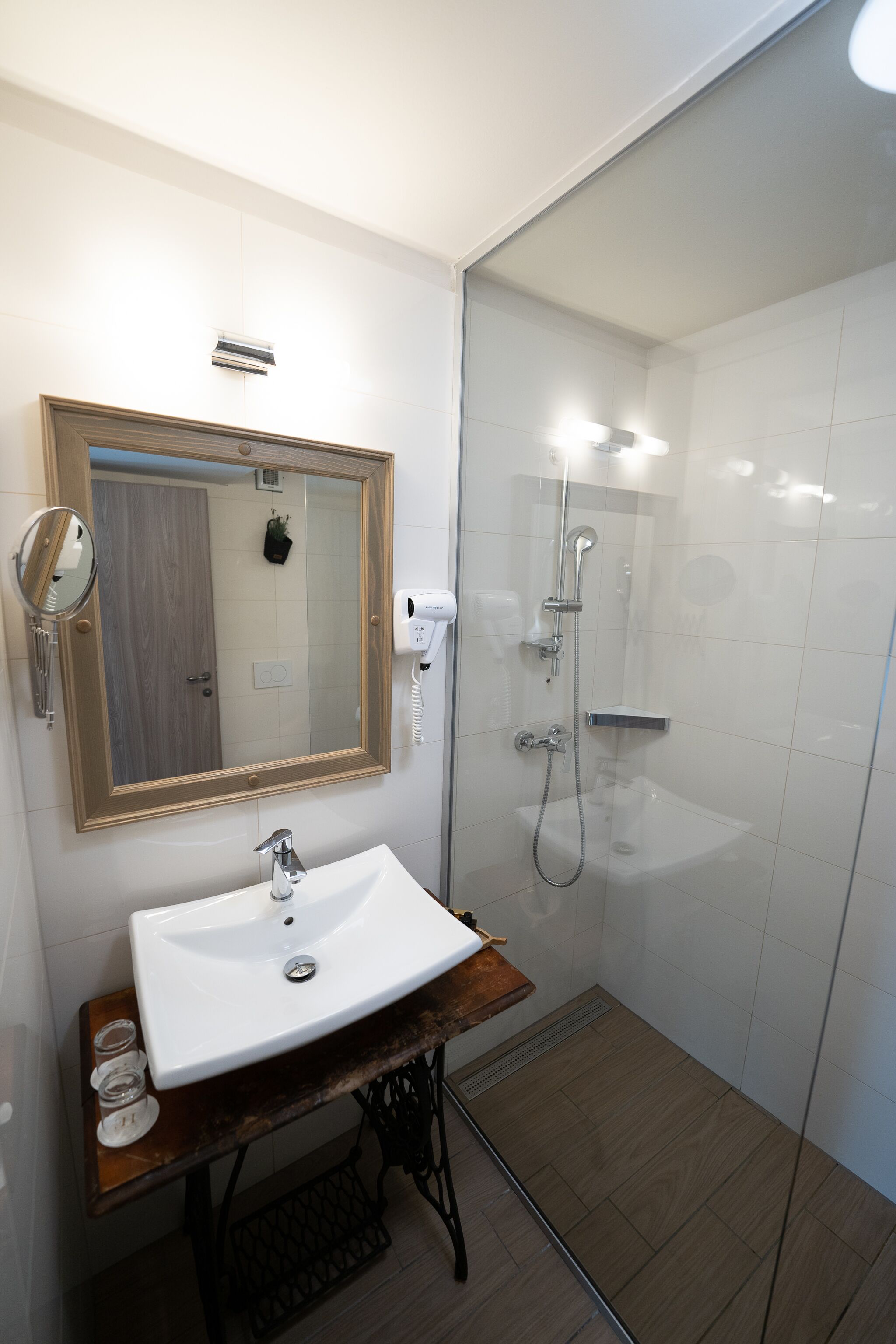 A bathroom with a white sink, wooden vanity, and a glass-enclosed shower.