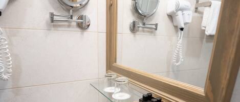 A bathroom with a white sink, two round mirrors, a glass shelf with toiletries, and a towel rack.