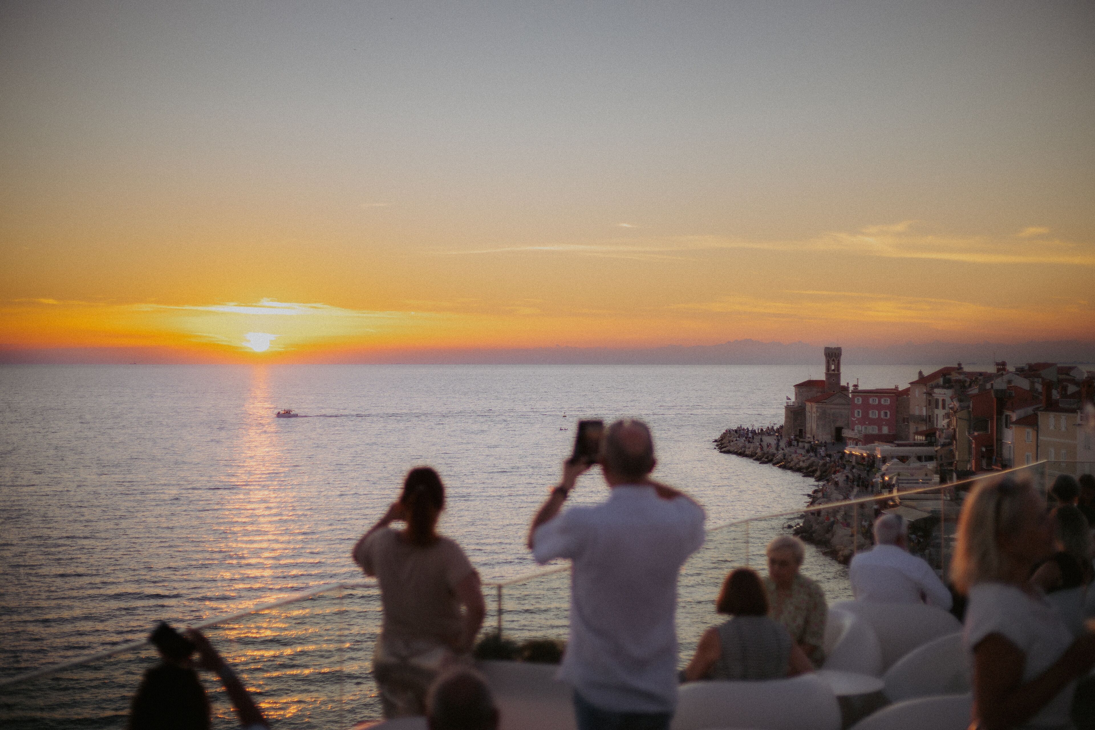 Vista al atardecer sobre un muelle, con gente fotografiando.