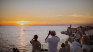 Une vue sur le coucher de soleil au-dessus d’un front de mer, où des personnes prennent des photos.