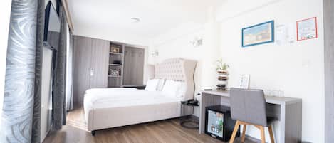 A modern hotel room with a bed, desk, chair, and a small trash bin.