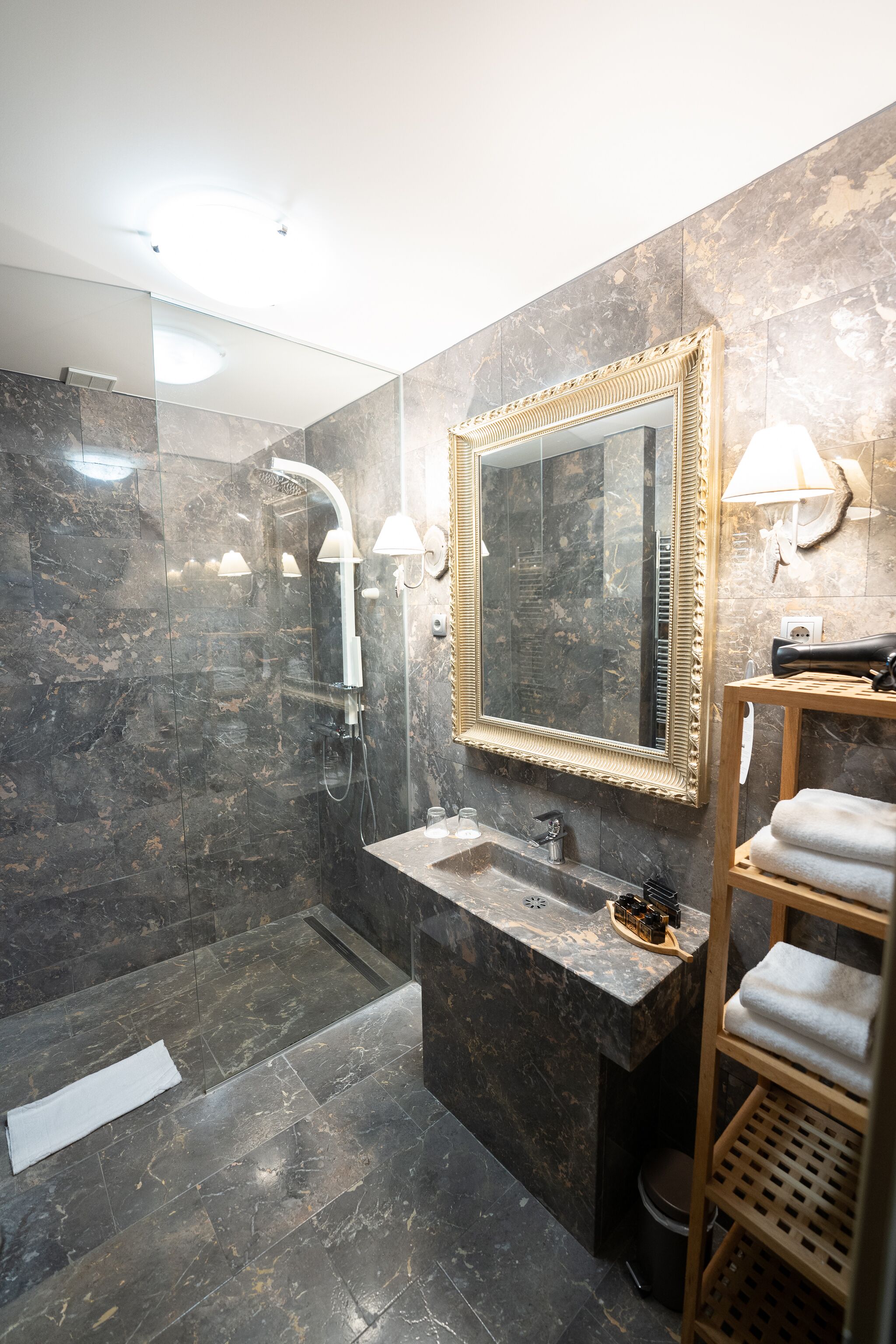 A modern bathroom with a glass-enclosed shower, a marble sink, and a large mirror with a gold frame.