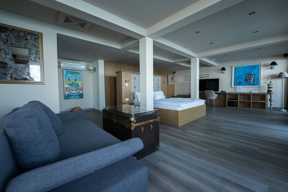 A modern hotel room with a large bed, a sofa, a desk, and a suitcase.