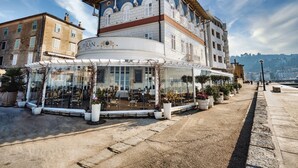 A hotel with a curved facade, large windows, and a terrace with potted plants. - Hotel Piran (Piran)