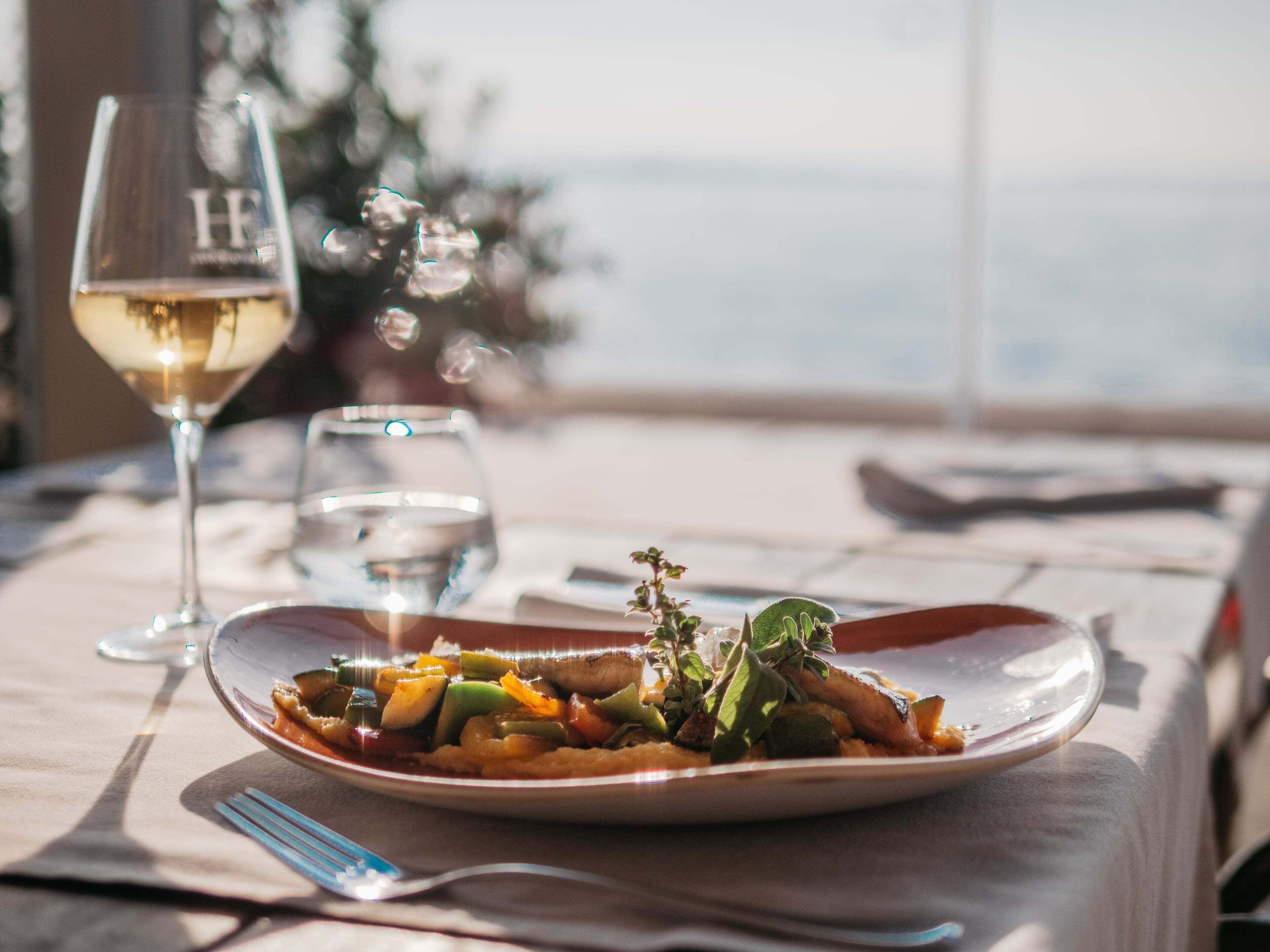 A dining table with a plate of food, a wine glass, and a water glass.