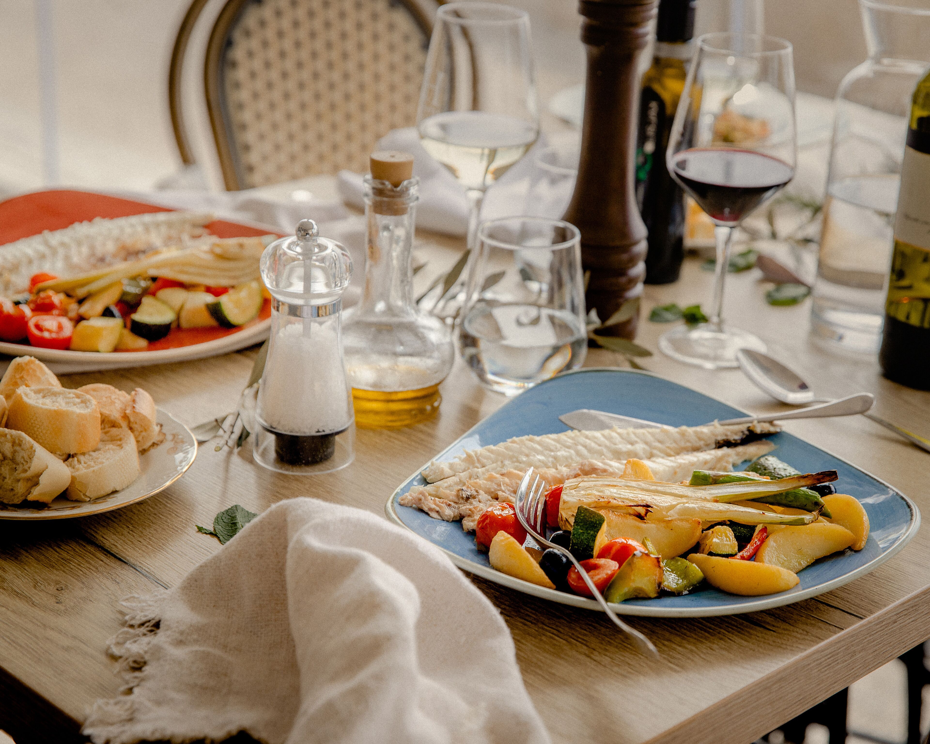 A dining table set with plates of food, glasses, and bottles, indicating a meal setting.