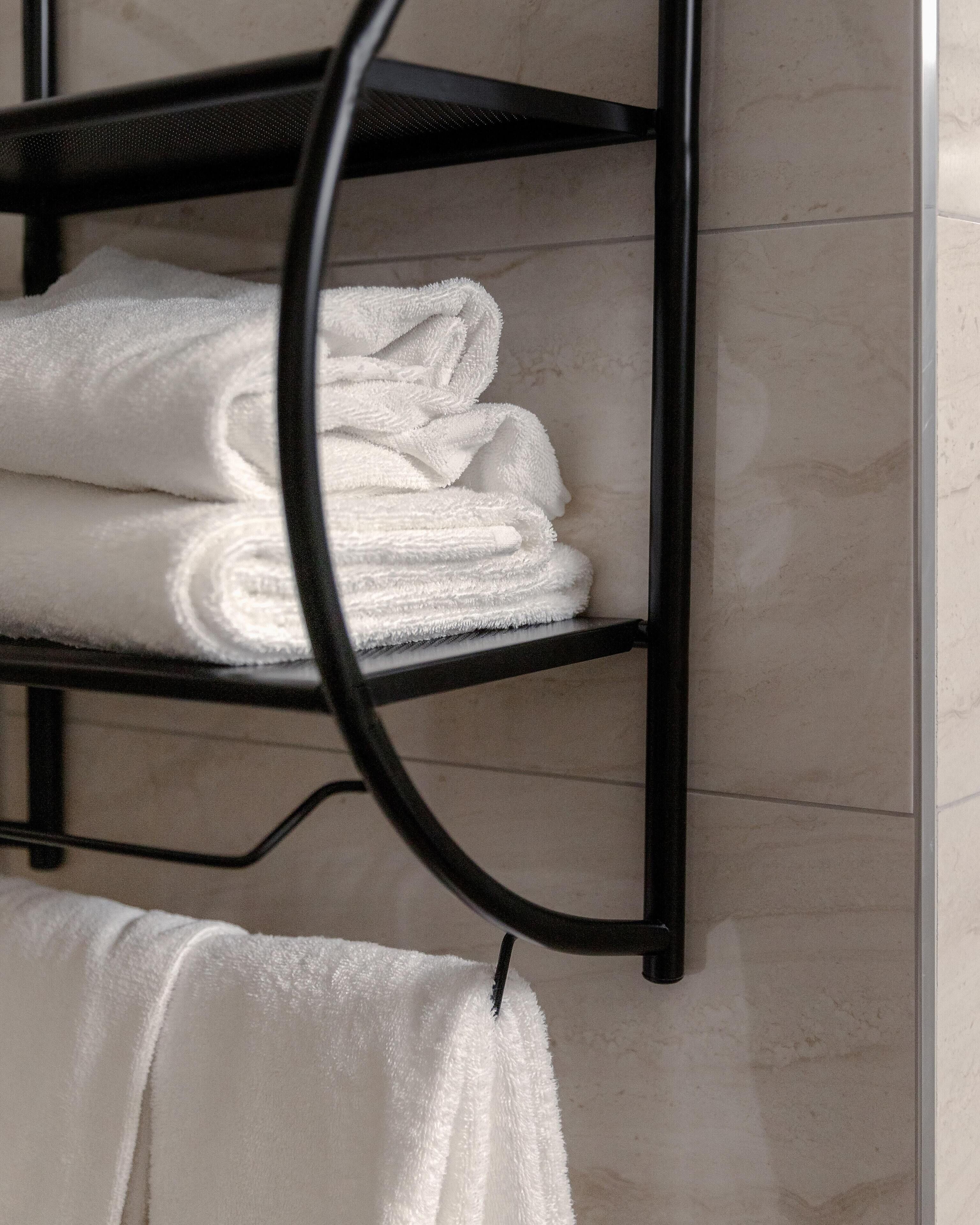 Une salle de bain avec un porte-serviettes en métal noir sur lequel sont soigneusement pliées des serviettes blanches.