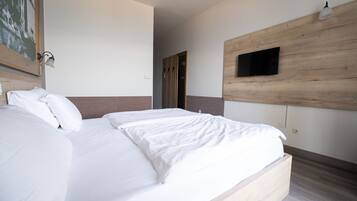 Una habitación de hotel moderna con una cama grande, un televisor de pantalla plana montado en un panel de madera y una puerta que da a otra habitación.