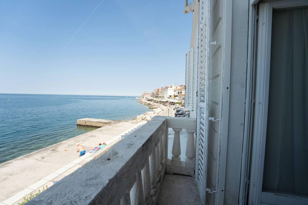 A balcony with a view of the sea and a row of buildings along the coast.