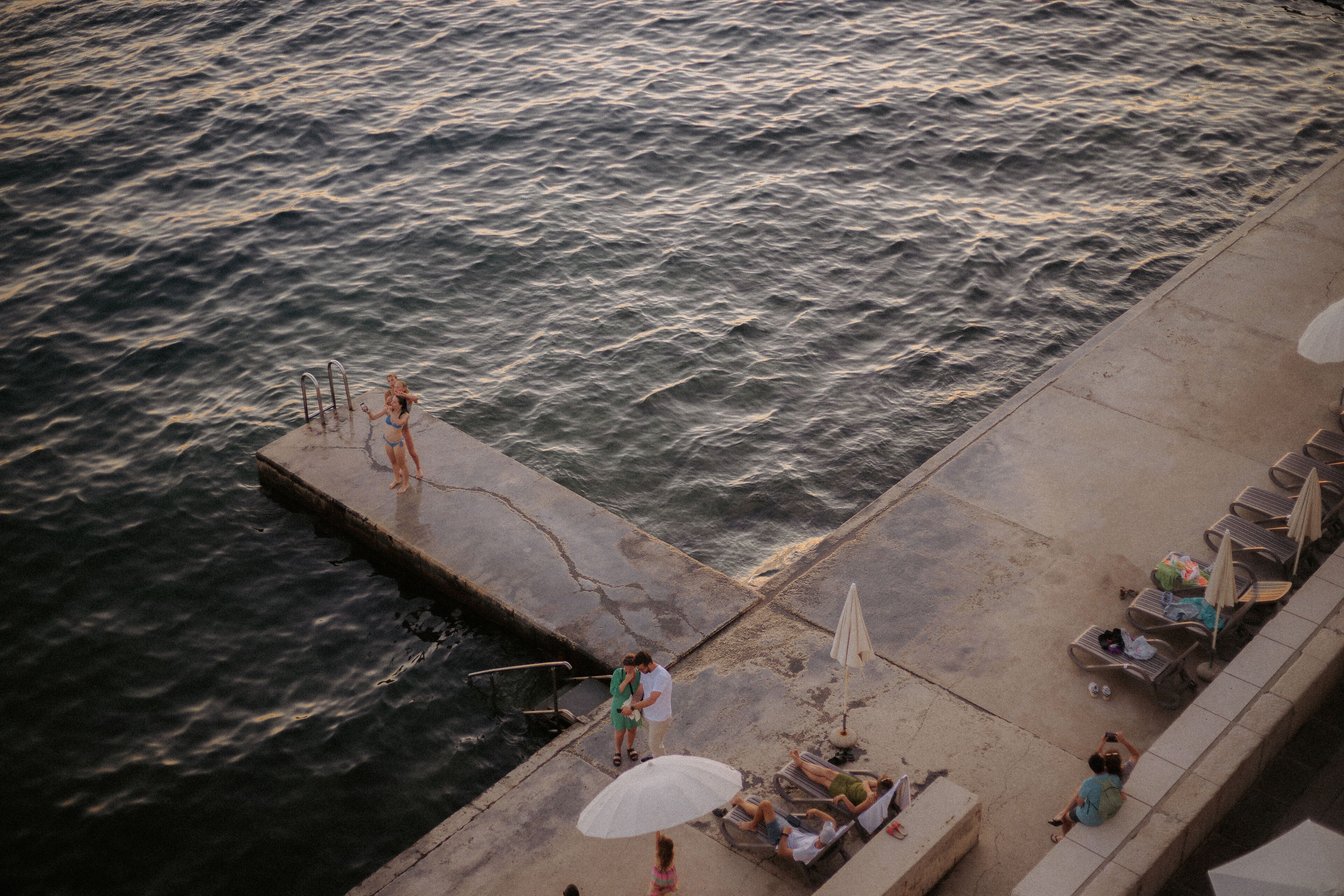 A pier with a concrete edge, a metal railing, and a row of lounge chairs with umbrellas.