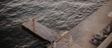 A pier with a concrete edge, a metal railing, and a row of lounge chairs with umbrellas.