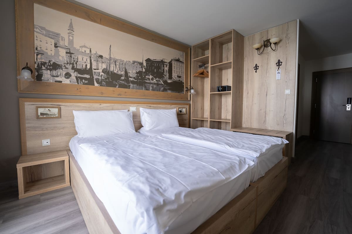 A bedroom with a large bed, wooden headboard, a cityscape painting, built-in shelves, and a wardrobe.