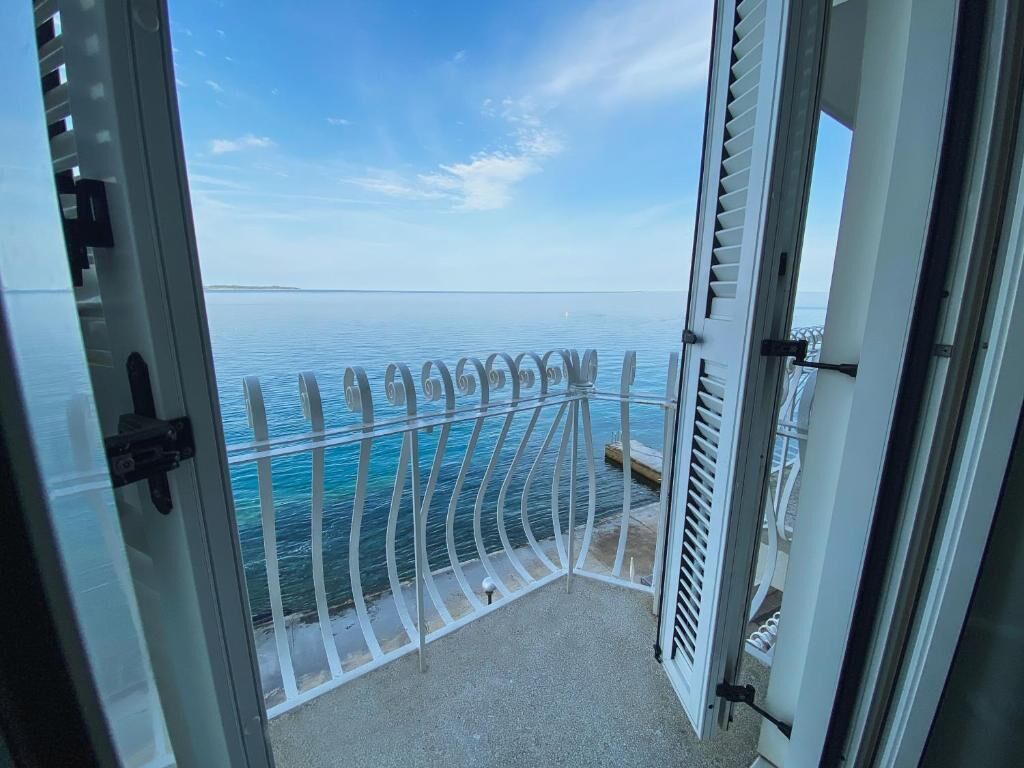 Een open balkon met een metalen hekwerk, uitkijkend op een rustige zee.