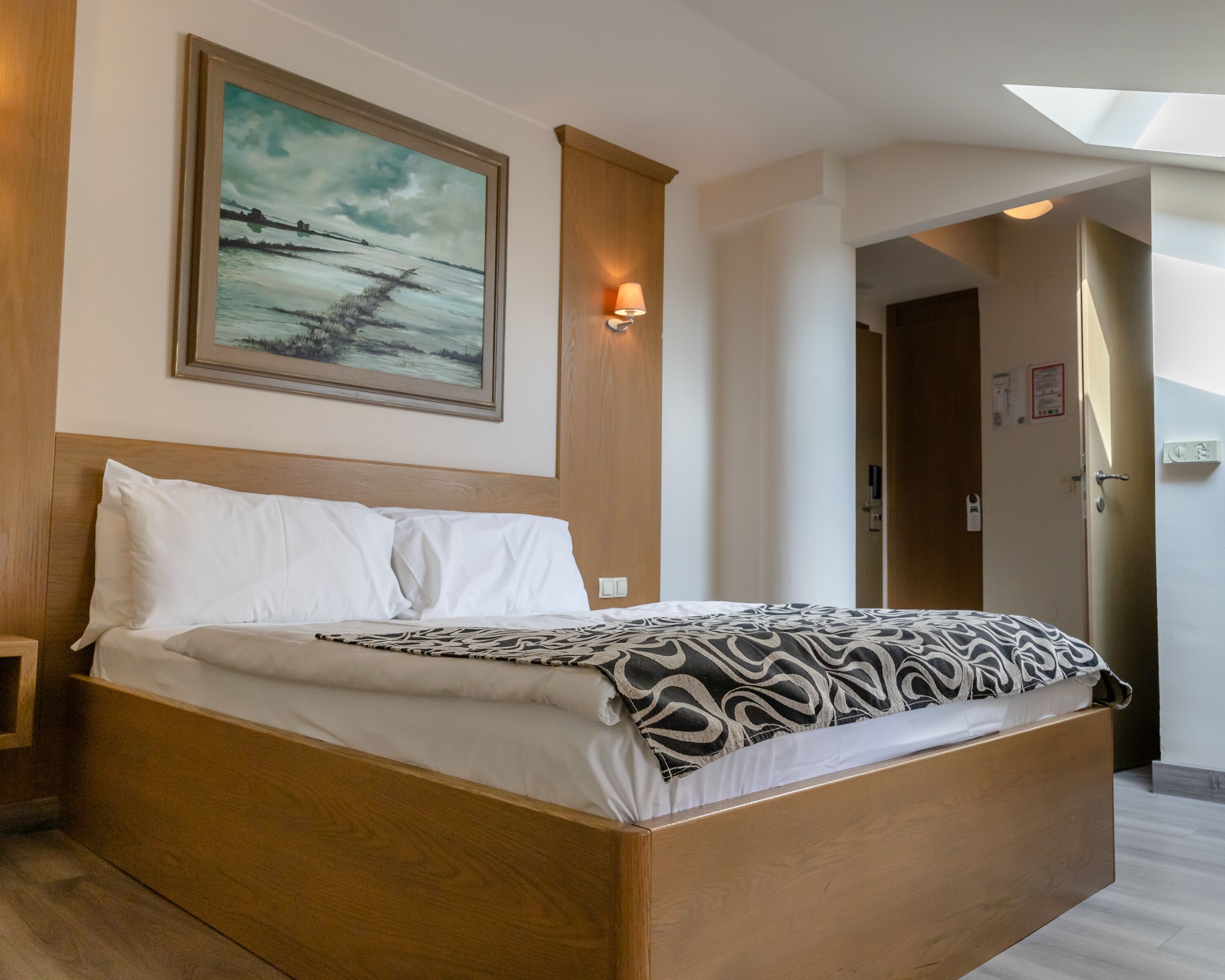 A hotel room with a large bed, a painting on the wall, a nightstand, and a lamp.