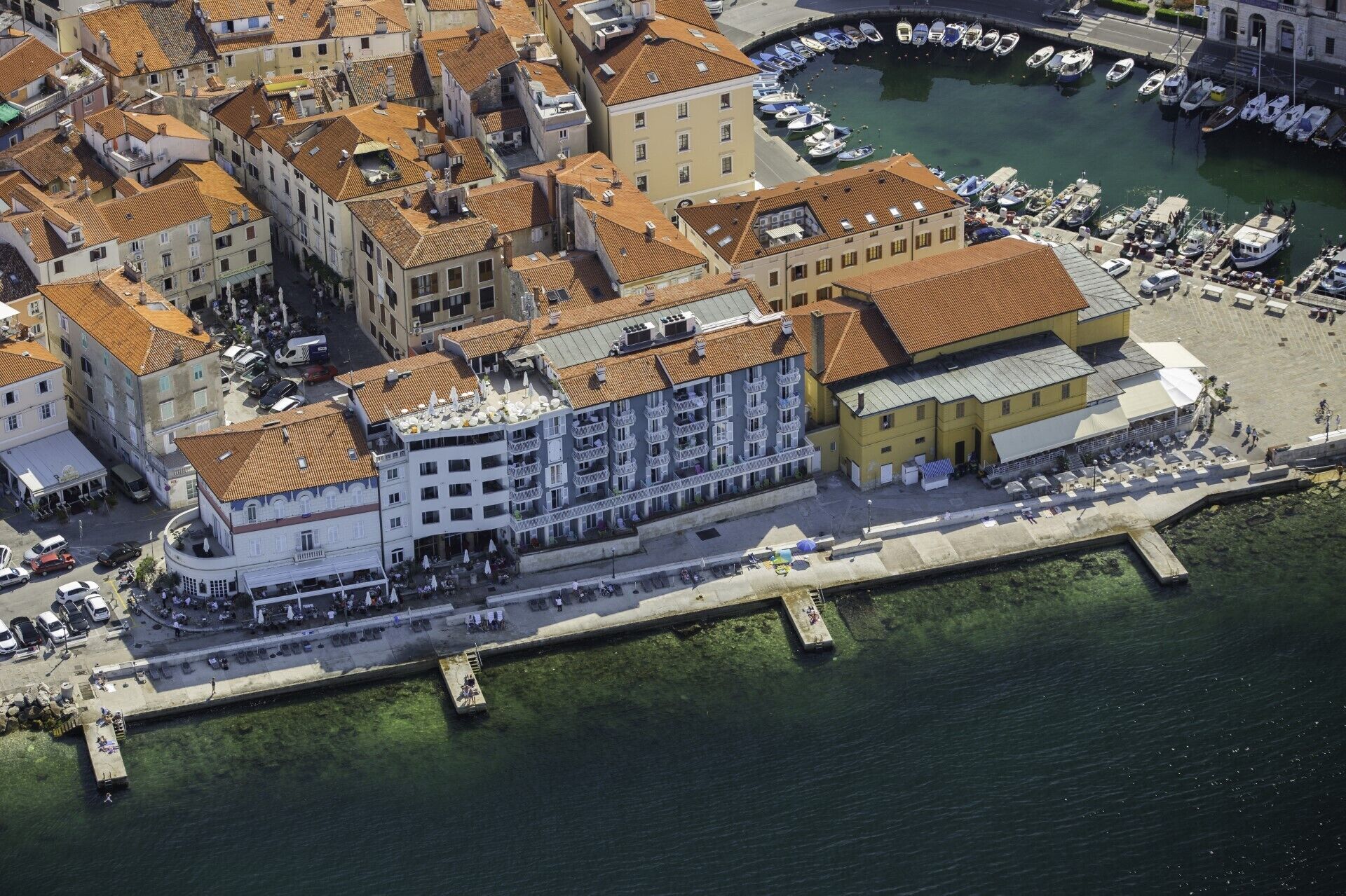 Una vista aerea di una cittadina costiera con un edificio di rilievo, balconi e un lungomare.