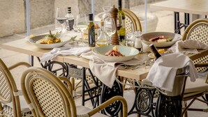 A table set for dining with a view of the sea, wicker chairs, and a variety of dishes and drinks. - Hotel Piran (Piran)