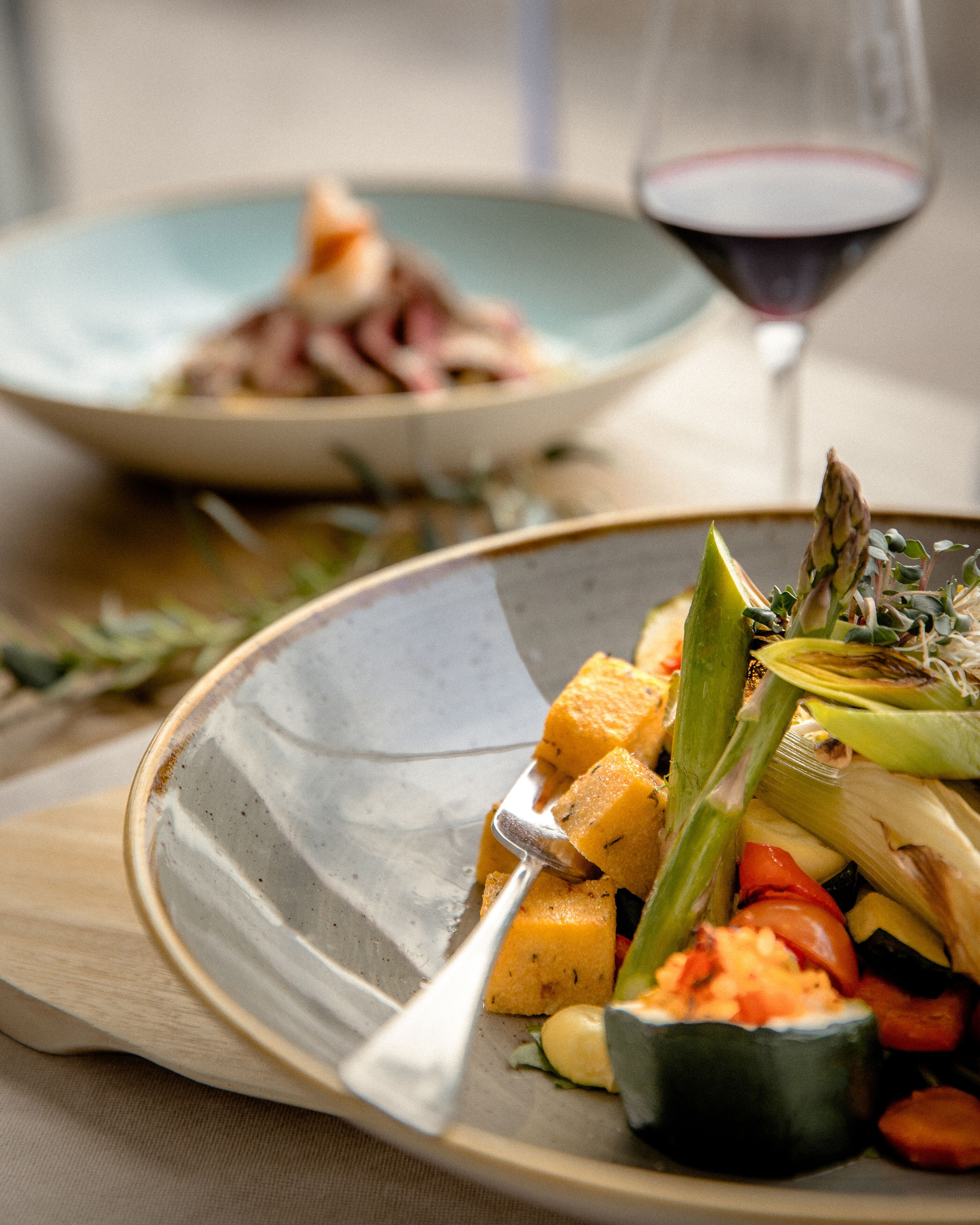 A dining table with a plate of food, a glass of red wine, and a fork.